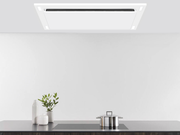 Matte white VICTORY Sunset range hood installed in a custom ceiling soffit box over a black induction cooktop, highlighting the perimeter suction panel and built-in LED lighting. bg__full