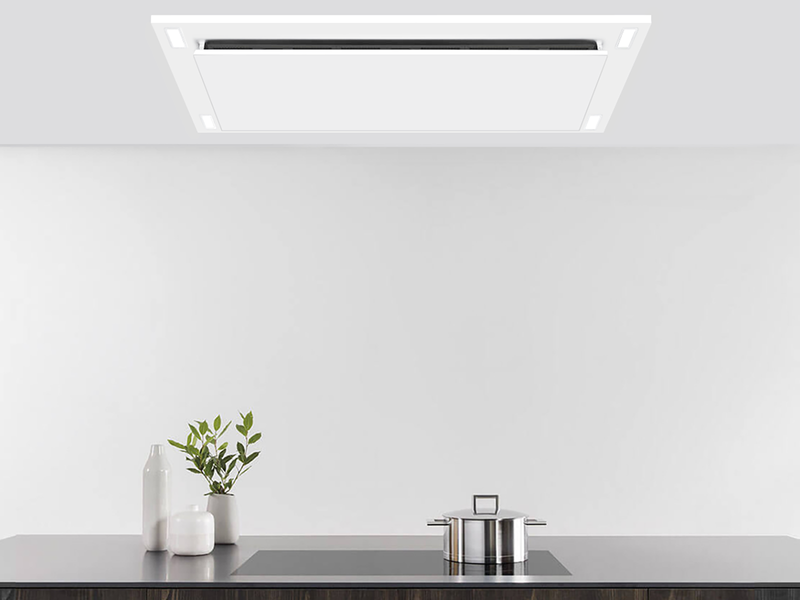 Matte white VICTORY Sunset range hood installed in a custom ceiling soffit box over a black induction cooktop, highlighting the perimeter suction panel and built-in LED lighting. bg__full